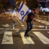 Seorang pengunjuk rasa merobohkan barikade sambil memegang bendera Israel selama unjuk rasa besar di Tel Aviv
